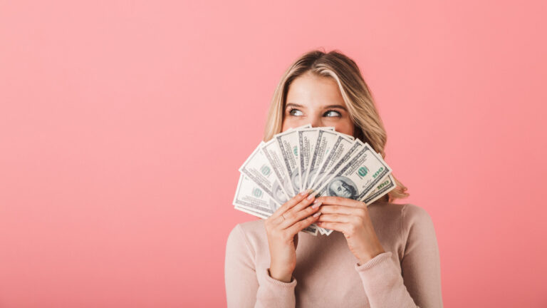 Lady holding money to her face and smiling with a pink background
