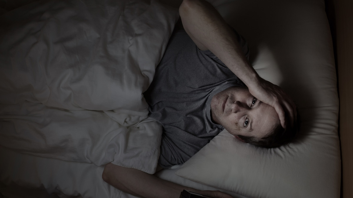 A man laying awake in bed at night frustrated