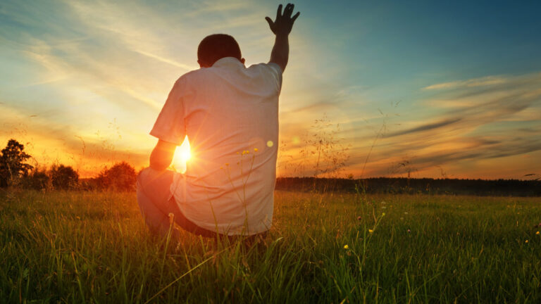 Man raising his arm praying towards the sun.