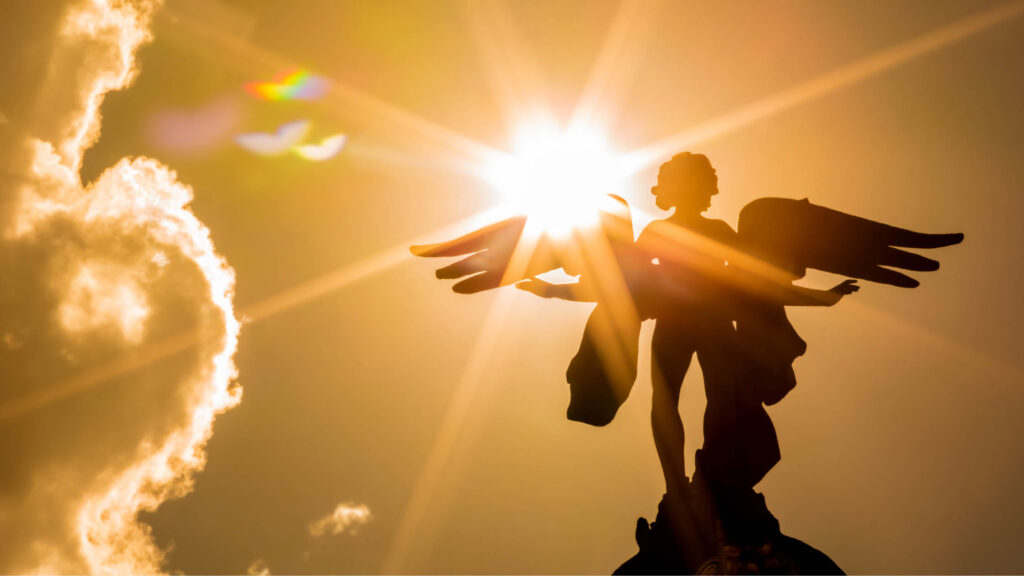 An angel statue in the sky with the sun beaming onto it.